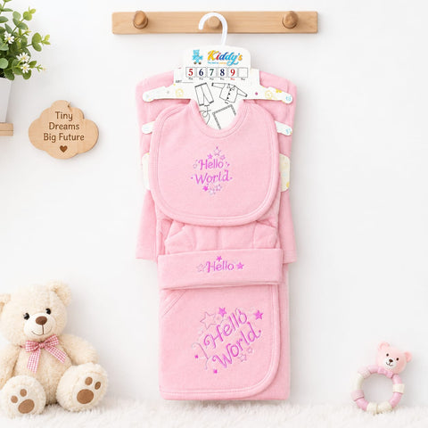 A pink baby clothing set hanging on a wooden hanger against a white wall, featuring a bib and matching footed towel with 'Hello World' text and star embroidery. A teddy bear sits on the left, and a small pink toy is on the right.