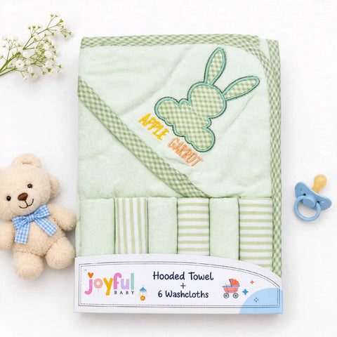 A folded light green hooded baby towel set with a bunny applique and the words 'APPLE CARROT' on the hood, shown with six matching washcloths. The set is packaged with a visible Joyful Baby label and styled on a white background with a teddy bear, baby fl