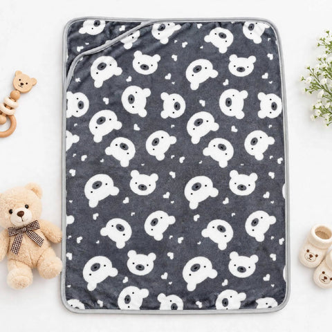 A square baby blanket or changing pad cover with a dark gray background and an all-over white teddy bear print, styled in a flat lay with a teddy bear, teething ring, and baby booties around it.