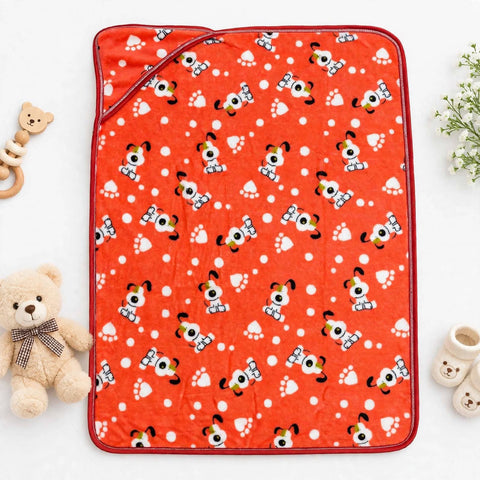 A red baby blanket with a playful pattern of cartoon dogs, hearts, and paw prints, styled in a flat-lay with a teddy bear, teething ring, and baby booties on a white background.