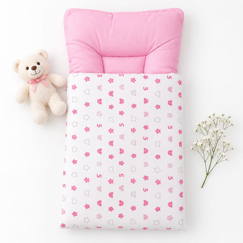 A baby sleep sack or quilt with a pink padded neck pillow, featuring a white base printed with pink hearts, stars, and crescent moons. The product is styled in a flat-lay arrangement with a small beige teddy bear on the left and baby's breath flowers on t