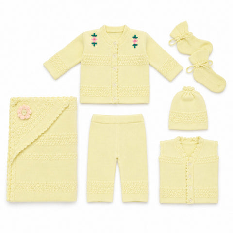 A coordinated baby knit clothing set laid out on a white background, including a cardigan, pants, hat, booties, and a blanket. The set is a pale buttery yellow with small embroidered floral details on the cardigan and a pink flower applique on the blanket