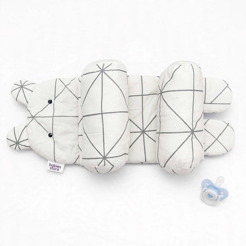A white baby sleep sack or quilted blanket with a gray geometric line pattern, shown on a white background next to a blue pacifier. A small tag on the left reads 'babies store'.