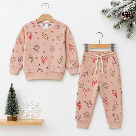 A children's two-piece clothing set consisting of a long-sleeve sweatshirt and matching jogger pants, both in a dusty pink color with an all-over ice cream cone print. The sweatshirt is shown on a wooden hanger, and the pants are shown on a metal hanger, 
