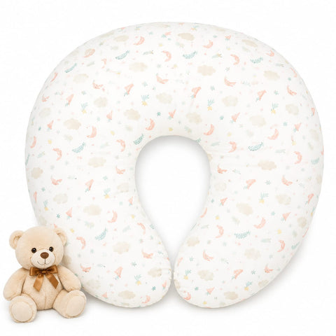 A U-shaped nursing pillow with a white background and a delicate pastel pattern of crescent moons, clouds, and stars, shown next to a small beige teddy bear toy on a white background.