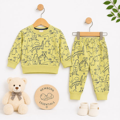 A baby clothing set displayed on wooden hangers against a white background, including a long-sleeve sweatshirt and matching jogger pants in a pale yellow-green color with black animal line drawings. A teddy bear, a round 'Newborn Essentials' card, and cre