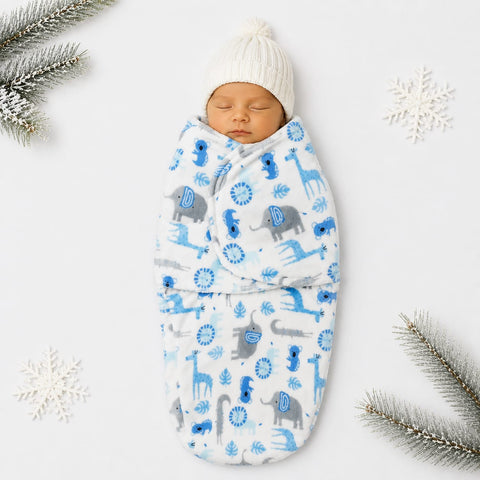 A sleeping newborn baby swaddled in a white wrap blanket with a blue and gray animal print, wearing a white knit pom-pom hat, styled on a white background with decorative snowflakes and pine branches.