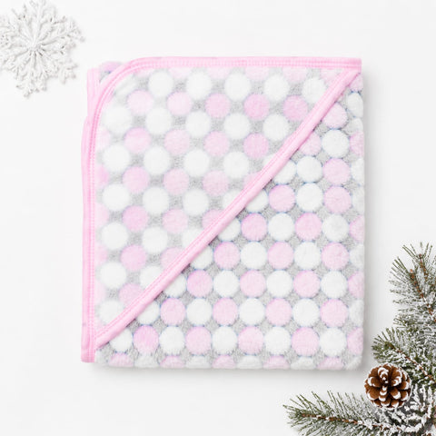 A folded hooded blanket with a pink and white polka dot pattern and a pink border, styled on a white background with decorative snowflake and pine elements.