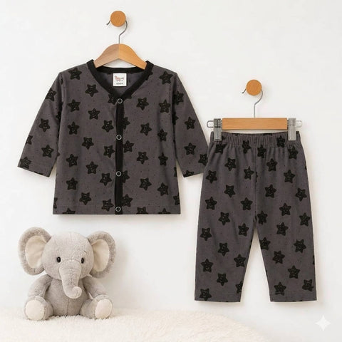 A baby clothing set consisting of a dark gray cardigan with black star print and matching pants, displayed on wooden hangers on a white wall, with a plush gray elephant toy on a white rug below.