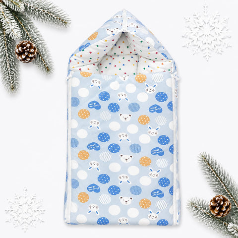 A baby hooded changing pad or burp cloth shown flat on a white background with decorative pine branches, pinecones, and white snowflakes. The fabric has a light blue base with white polka dots, blue polka dots, orange polka dots, and small cartoon animal 