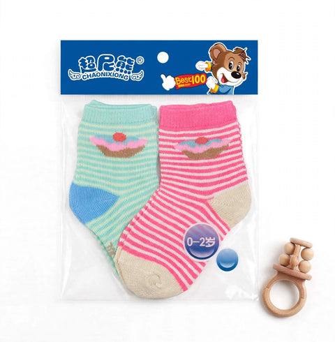 A pair of baby socks in a clear plastic package with a blue header card featuring a cartoon bear and Chinese branding. The socks are striped in mint green and pink, each with a small cupcake motif, and are shown alongside a wooden teether on a white backg