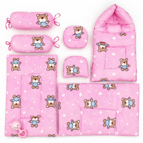 A coordinated baby bedding and accessory set in pink, featuring a teddy bear print. The set includes a baby blanket, a sleeping bag, a changing pad, two cylindrical pillow covers with tie loops, a round cushion, a small folded cushion, and a pink teething