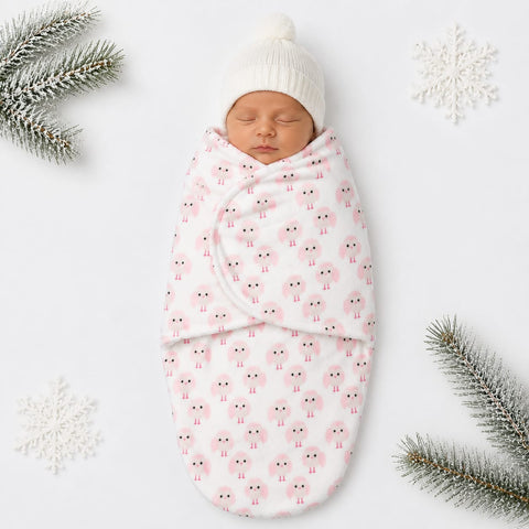 A sleeping newborn baby swaddled in a white blanket with a pink sheep pattern, wearing a white knit beanie hat, styled on a white background with decorative snowflakes and pine branches.