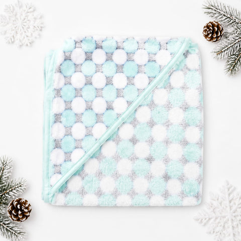 A square baby blanket with a diagonal hood, featuring a pattern of mint green, white, and light gray polka dots, styled on a white background with holiday pine branches and snowflakes.