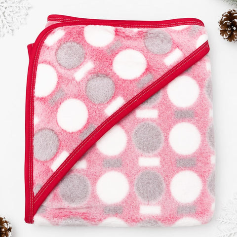 A folded plush hooded blanket in pink, white, and gray with a red border, photographed on a white background with small decorative holiday props in the corners.