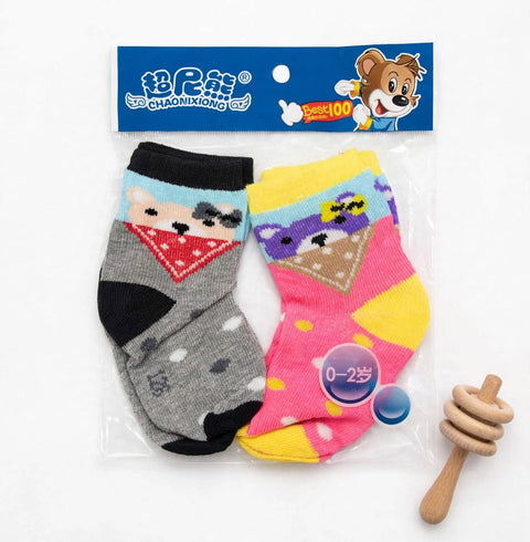 A pair of children's novelty socks in clear plastic packaging with a blue header card, shown alongside a small wooden honey dipper toy on a white background. The socks feature cartoon animal faces: one gray sock with a bear face and red bandana, and one p
