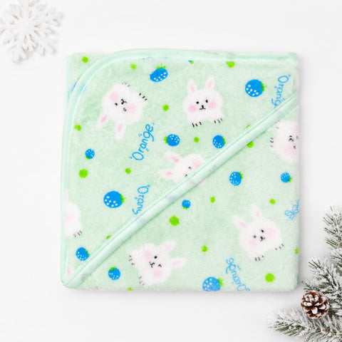 A light mint green hooded baby towel with a pattern of white bunnies, blue and green dots, and blue script text spelling 'Orange' and 'Sweet', laid flat on a white background with holiday decorations in the corners.