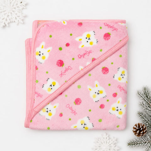 A folded pink hooded towel with a bunny and strawberry print, styled on a white background with decorative snowflake and pine elements.