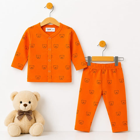 A baby two-piece outfit set consisting of an orange long-sleeve cardigan and matching pants, both printed with a small teddy bear face pattern. The cardigan is shown on a wooden hanger, the pants on a gray hanger, and a plush teddy bear sits on the floor 