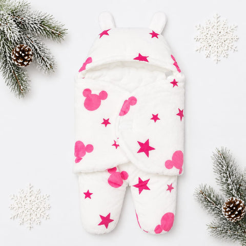 A white footed baby sleeper with pink Mickey Mouse-style shapes and stars, photographed flat on a white background with decorative pine branches and snowflakes around it.