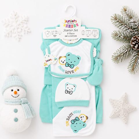 A baby starter set laid flat on a white background with seasonal props. The set includes a long-sleeve romper, a bib, and a hat in mint green and white, decorated with cartoon bear graphics and the words 'PRAISE LOVE ME' and 'HAPPY BIRTH'.