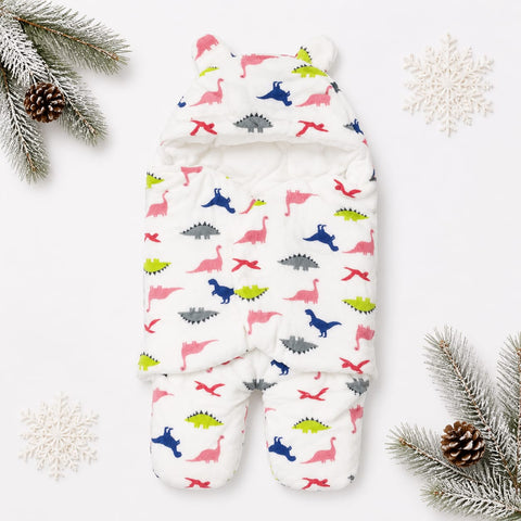 A white hooded baby sleeper with a colorful dinosaur print, styled in a flat lay with pine branches, snowflakes, and pinecones on a white background.
