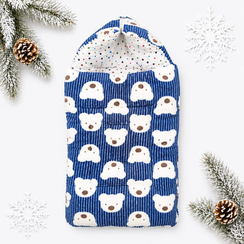 A blue corduroy baby swaddle blanket with a white polar bear face pattern, styled with white snowflakes and pinecones on a white background.