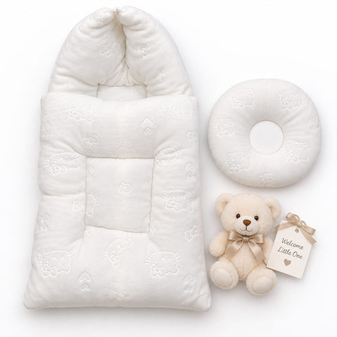 A white quilted baby sleep bag with a hood, a matching white circular baby pillow, and a small cream teddy bear with a 'Welcome Little One' tag, arranged on a clean white background.