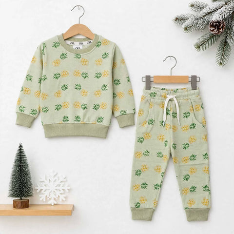 A children's two-piece outfit set consisting of a long-sleeve sweatshirt and jogger pants, both in a light sage green color with a yellow pineapple print. The sweatshirt is shown on a wooden hanger, and the matching pants are shown on a metal hanger, set 