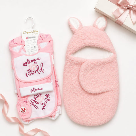 Pink baby gift set including a plush bunny hooded bootie and a folded matching outfit with a white bib that reads 'Welcome to the World' on a white background, styled with a gift box and ribbon.