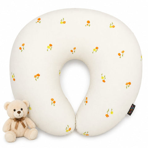 A U-shaped baby nursing pillow in off-white with a small orange and yellow floral pattern, shown on a white background next to a small beige teddy bear toy.