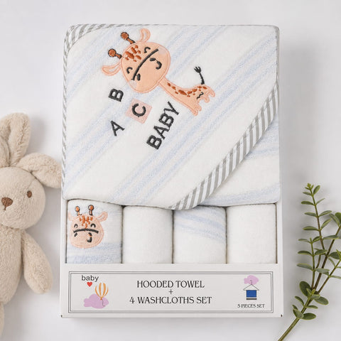 A boxed baby towel set displayed on a white background, with a plush bunny on the left and a green sprig on the right. The set includes a hooded towel with a giraffe illustration and the words 'BABY' on the hood, plus three folded washcloths inside.