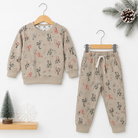 A children's two-piece pajama set consisting of a long-sleeve sweatshirt and matching jogger pants, displayed on wooden hangers against a white background with small holiday props including a pine branch, pinecone, miniature tree, and snowflake.