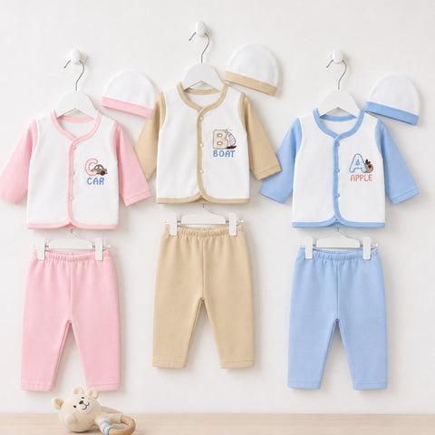 Three baby clothing sets hanging on white hangers against a light wall, each consisting of a sleeveless zip-front vest, pants, and hat. The left set is white and pink with a pink hat; the center set is cream and tan with a tan hat; the right set is white 