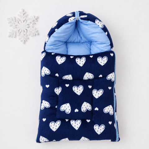 A navy blue hooded baby sleeping bag or pouch with a white heart pattern, shown flat on a light gray background with a white snowflake decoration in the top left corner.