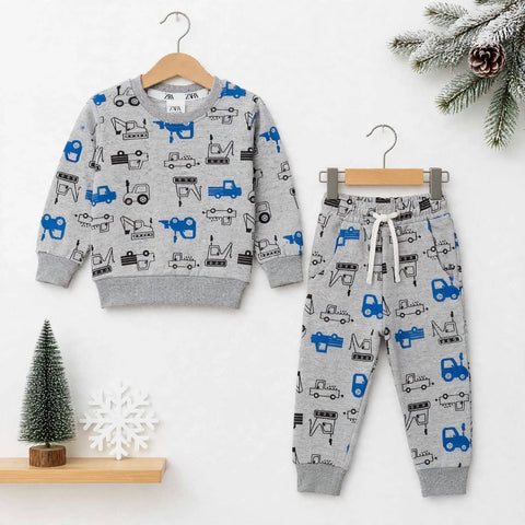 A children's two-piece clothing set displayed on wooden hangers against a white wall. The set includes a long-sleeve sweatshirt and matching jogger pants, both in heather gray with an all-over print of blue and black construction vehicles.