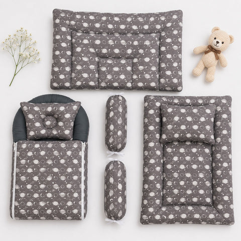 A baby bedding set arranged on a white background, including a changing pad, mattress, footmuff, two cylindrical bolsters, and a matching pillow, all in a gray fabric with a white cloud pattern. A small teddy bear and baby's breath sprig are placed as sty