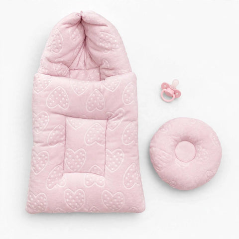 A light pink baby sleep sack with a hood and a matching round cushion, both featuring a quilted heart pattern, displayed on a clean white background next to a pink pacifier.