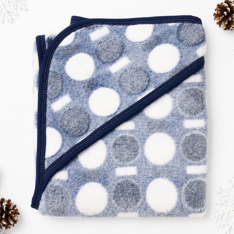A folded fleece blanket with a blue-gray and white polka dot pattern and navy blue trim, styled on a white background with decorative pinecones in the corners.