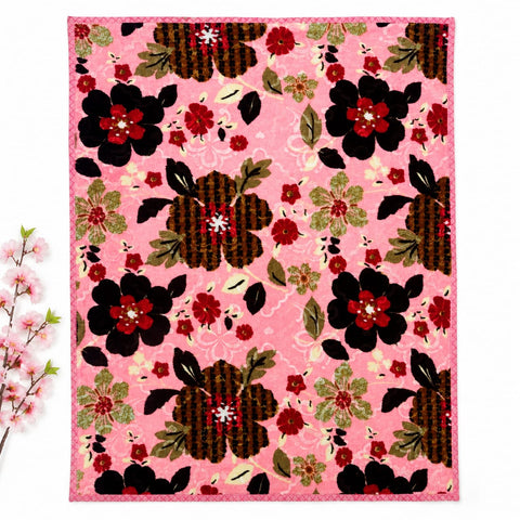 A square textile product, likely a quilt or rug, featuring a vibrant pink background with a repeating floral pattern of black, red, and olive green flowers. The textile is displayed flat against a white background with a decorative cherry branch on the le