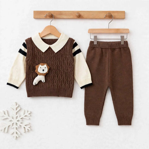 A baby clothing set displayed on wooden hangers against a light background. The set includes a brown cable-knit vest with cream sleeves, black sleeve stripes, a cream collar, and a small lion applique on the chest, paired with matching brown pants.