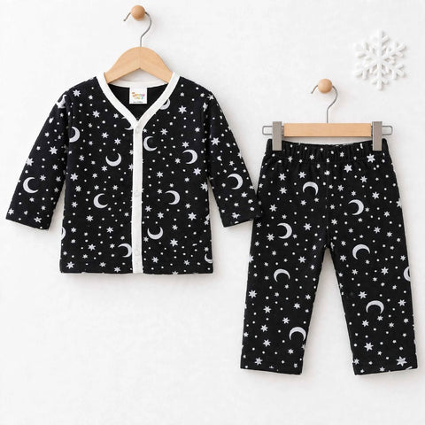 A baby two-piece pajama set featuring a long-sleeve cardigan and pants in black with a white celestial print of stars and crescent moons, displayed on wooden hangers against a white textured wall.